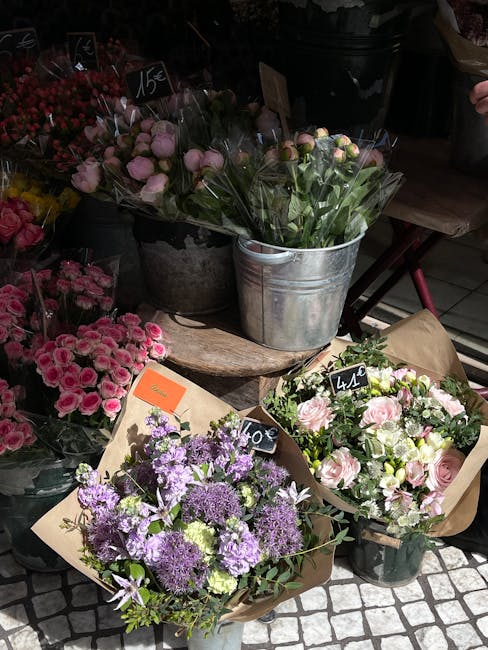 A display of fresh floral bouquets arranged on a rustic wooden table, featuring a variety of flowers including pink roses, purple statice, and light pink peonies, all wrapped in brown kraft paper with